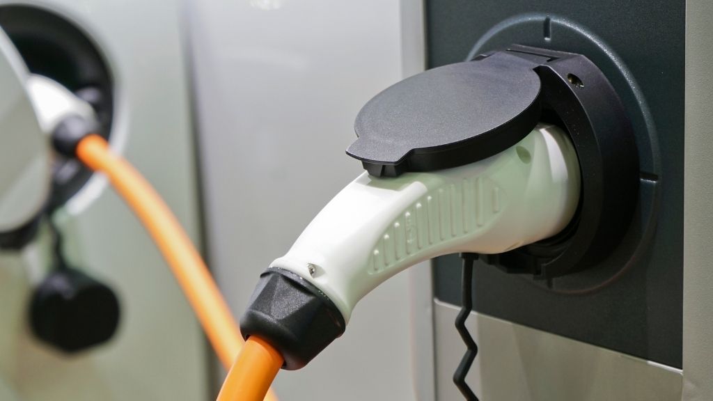 Elbilsladdare med orange sladd från laddstation till vit bil